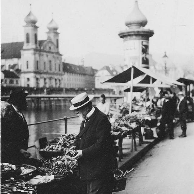 Schwarz-Weiss-Aufnahme eines älteren Mannes mit Hut an einem Markt an einem Fluss. Schwarz-Weiss-Aufnahme eines älteren Mannes mit Hut an einem Markt an einem Fluss.