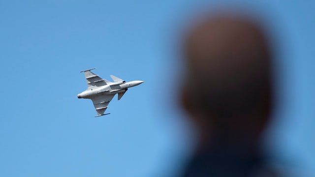 Ein Kampfflugzeug fliegt und im Vordergrund ist eine Silhouette einer Person. Ein Kampfflugzeug fliegt und im Vordergrund ist eine Silhouette einer Person.
