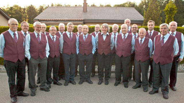 Eine Reihe mit in Weste gekleideter Chorsängerinnen und Chorsänger. Eine Reihe mit in Weste gekleideter Chorsängerinnen und Chorsänger.