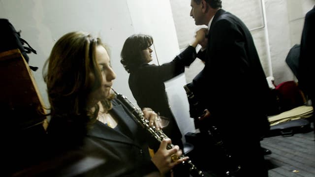 Im Probenraum des Irakischen Symphonie Orchesters: Im Vordergrund spielt eine Frau Klarinette, im Hintergrund wird einem Mann die Krawatte gebunden. Im Probenraum des Irakischen Symphonie Orchesters: Im Vordergrund spielt eine Frau Klarinette, im Hintergrund wird einem Mann die Krawatte gebunden.