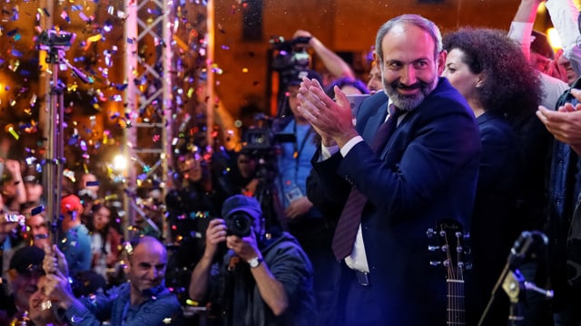 Paschinjan auf einer Bühne klatscht in die Hände, dazu fällt Glitter von oben herab. Paschinjan auf einer Bühne klatscht in die Hände, dazu fällt Glitter von oben herab.