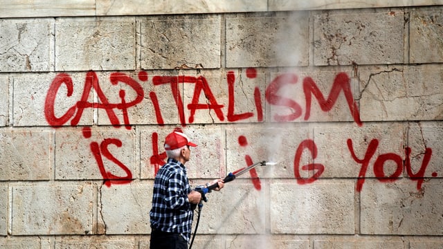 Ein Arbeiter entfernt die Graffitti-Aufschrift «Capitalism is killing you» von einer Mauer in Athen. Ein Arbeiter entfernt die Graffitti-Aufschrift «Capitalism is killing you» von einer Mauer in Athen.