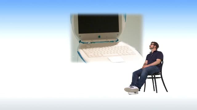 Guido Berger sitzt auf einem Stuhl und schaut ein Bild eines alten Computers an. Guido Berger sitzt auf einem Stuhl und schaut ein Bild eines alten Computers an.