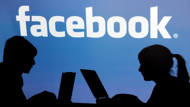 Zwei Menschen am Computer, dahinter Facebook-Logo Zwei Menschen am Computer, dahinter Facebook-Logo