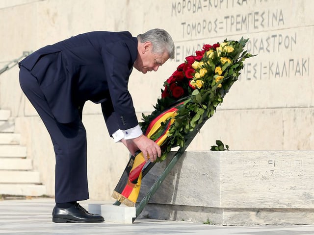 Ein Mann im dunklen Anzug legt einen grossen Blumenkranz nieder. Ein Mann im dunklen Anzug legt einen grossen Blumenkranz nieder.
