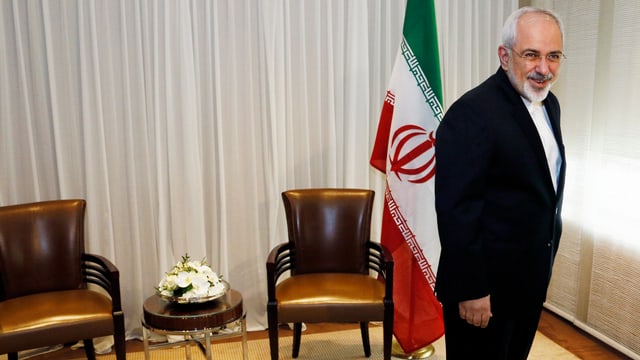 Irans Aussenminister Sarif stehend vor zwei Sesseln und einer iranischen Fahne. Irans Aussenminister Sarif stehend vor zwei Sesseln und einer iranischen Fahne.