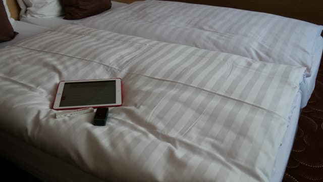 Tablet, Doppelmeter und Messgerät liegen auf dem Hotelbett. Tablet, Doppelmeter und Messgerät liegen auf dem Hotelbett.