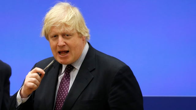 Johnson spricht in ein Mikrofon vor blauem Hintergrund. Johnson spricht in ein Mikrofon vor blauem Hintergrund.