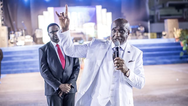 Pastor David Ibiyeomie trägt einen weissen Anzug. Er hält eine Hund an die Luft. Pastor David Ibiyeomie trägt einen weissen Anzug. Er hält eine Hund an die Luft.