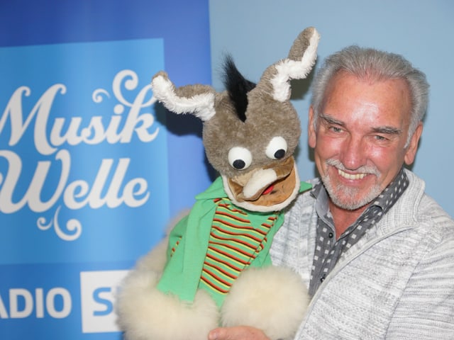 Kliby mit Handpuppe Caroline vor Musikwelle Logo. Kliby mit Handpuppe Caroline vor Musikwelle Logo.