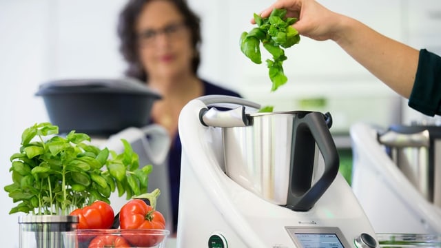Eine Person gibt Basilikum in einen Thermomix. Eine Person gibt Basilikum in einen Thermomix.