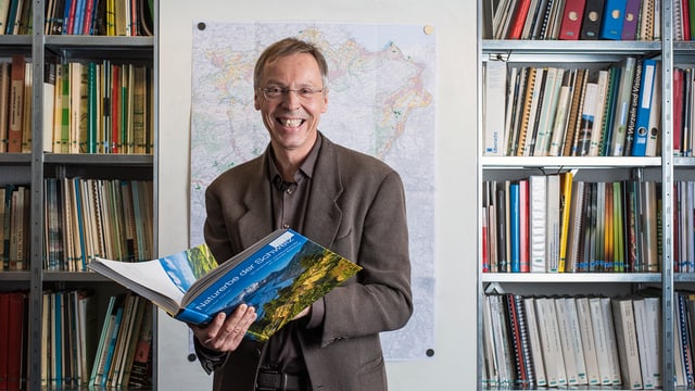 Raimund Rodewald steht mit einem Buch in seinem Büro. Raimund Rodewald steht mit einem Buch in seinem Büro.