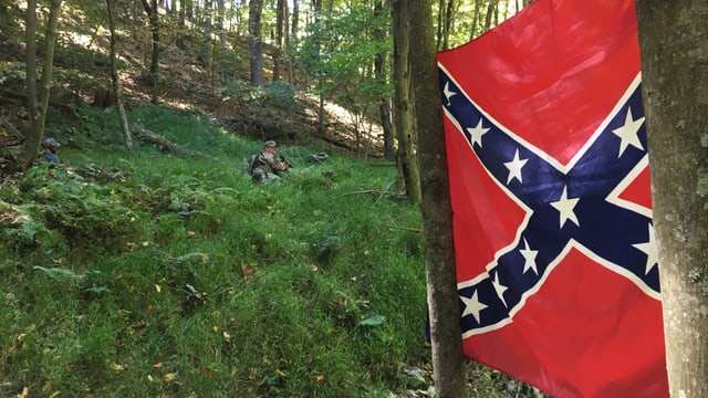Ein Miliz-Soldat liegt im Wald, daneben hängt die Konföderierten-Flagge. Ein Miliz-Soldat liegt im Wald, daneben hängt die Konföderierten-Flagge.