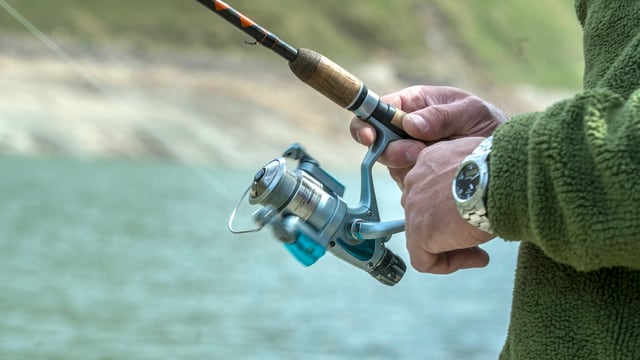 Ein Mann dreht an einer Kurbel der Fischerrute Ein Mann dreht an einer Kurbel der Fischerrute