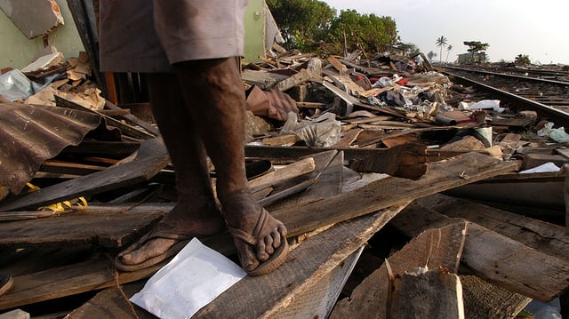 Schwarze Füsse stehen auf einem vom Tsunami verwüsteten Gebiet. Schwarze Füsse stehen auf einem vom Tsunami verwüsteten Gebiet.