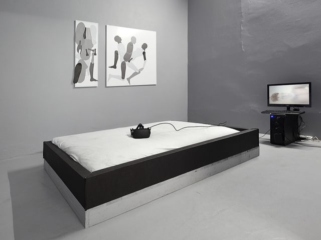Ein Bett, darauf eine virtual Reality Brille, dahinter ein Bildschirm. Ein Bett, darauf eine virtual Reality Brille, dahinter ein Bildschirm.