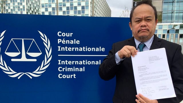 Ein Mann mit einem Schreiben in der Hand vor dem Schild des Internationalen Strafgerichtshofs. Ein Mann mit einem Schreiben in der Hand vor dem Schild des Internationalen Strafgerichtshofs.