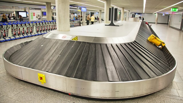 Ein Gepäcklaufband am Flughafen mit einer gelben Tasche darauf.