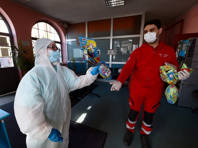 Frau im Schutzkleidung gibt Mann in Schutzkleidung ein Osterei