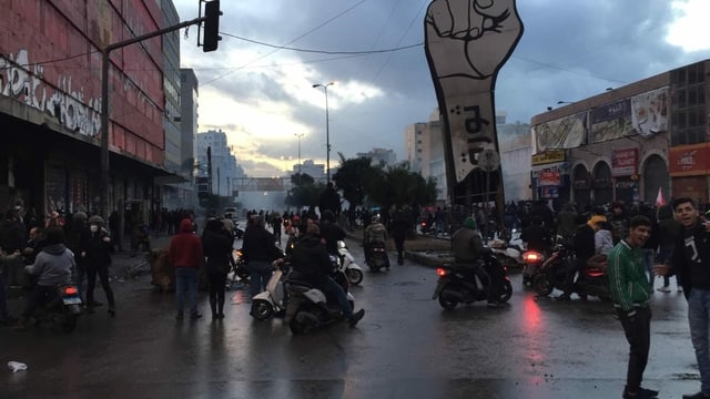 Personen auf der Strasse von Tripoli vor einem Plakat mit einer geballten Faus. Personen auf der Strasse von Tripoli vor einem Plakat mit einer geballten Faus.