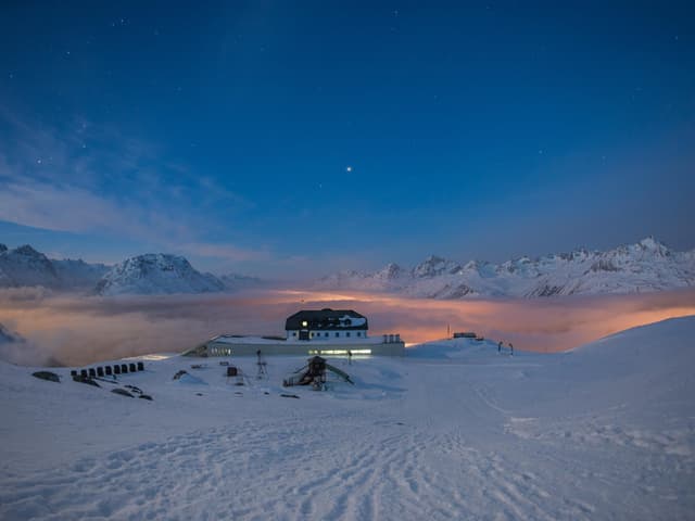 Blick von einem Berg auf eine Bergstation und das beleuchtete Nebelmeer.