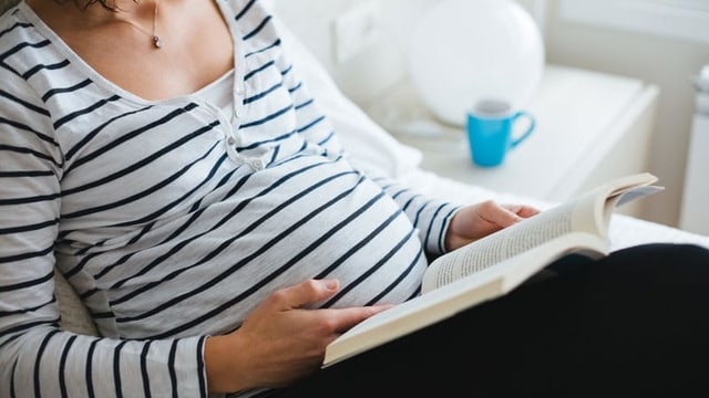 Eine kopflose schwangere Frau liest ein Buch.