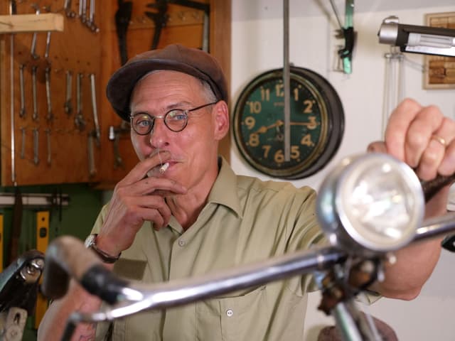 Ein rauchender Mann mit Mütze, seine linke Hand lehnt lässig auf einem alten Fahrradlenker. Ein rauchender Mann mit Mütze, seine linke Hand lehnt lässig auf einem alten Fahrradlenker.