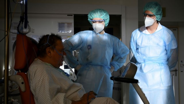 Patient mit Schlauch, eine Frau und ein Mann in Schutzkleidung Patient mit Schlauch, eine Frau und ein Mann in Schutzkleidung