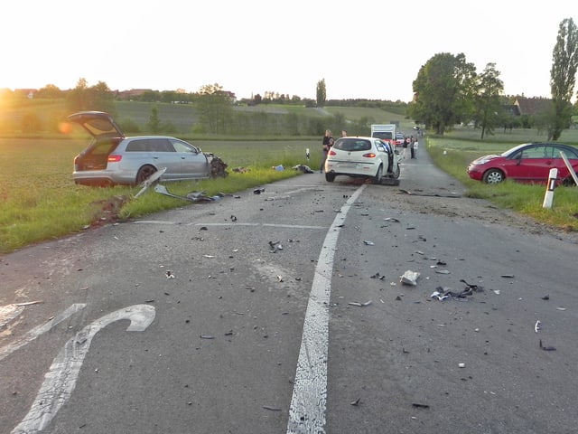 Eine Strasse mit drei Autos. Zwie der Autos befinden sich auf den Wiesen, die sich links und rechts der Strasse befinden. Eine Strasse mit drei Autos. Zwie der Autos befinden sich auf den Wiesen, die sich links und rechts der Strasse befinden.