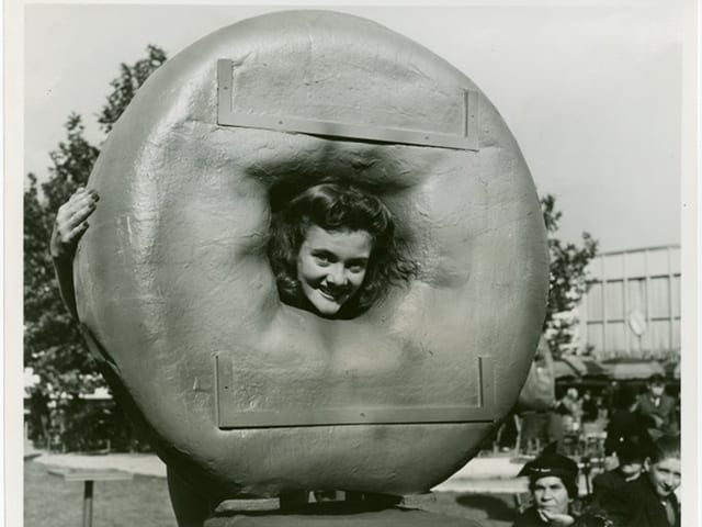 Eine Frau steckt ihren Kopf durch einen überdimensionalen, künstlichen Donut Eine Frau steckt ihren Kopf durch einen überdimensionalen, künstlichen Donut