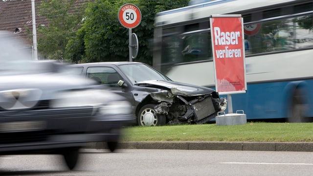 Ein Unfallauto steht auf einem Mittelstreifen, daneben ein Plakat mit der Aufschrift "Raser verlieren". Ein Unfallauto steht auf einem Mittelstreifen, daneben ein Plakat mit der Aufschrift "Raser verlieren".