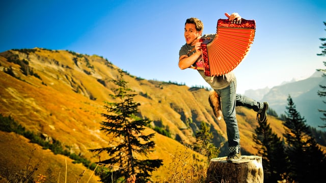 Marc A Trauffer mit Handorgel auf einem Baumstrunk in den Bergen. Marc A Trauffer mit Handorgel auf einem Baumstrunk in den Bergen.