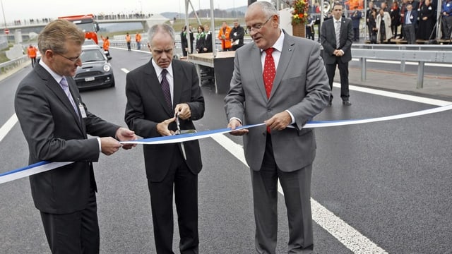 Drei Männer stehen auf der Autobahn und zerschneiden ein Band. Drei Männer stehen auf der Autobahn und zerschneiden ein Band.