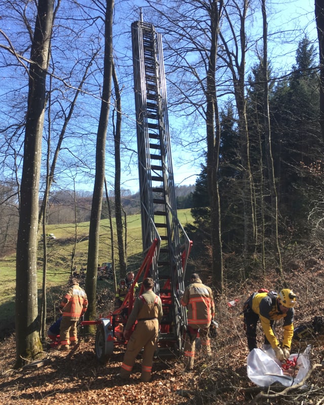Mehrere Männer in Schutz-Uniformen stehen um eine ausziehbare Leiter herum. Mehrere Männer in Schutz-Uniformen stehen um eine ausziehbare Leiter herum.