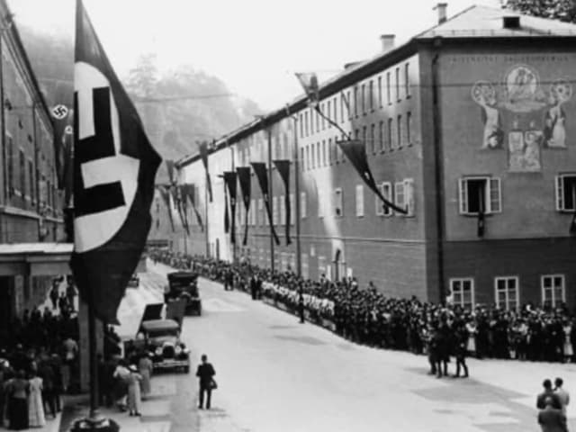 Strasse mit Haus, gesäumt von Menschen und Fahnen mit dem Hakenkreuz Strasse mit Haus, gesäumt von Menschen und Fahnen mit dem Hakenkreuz