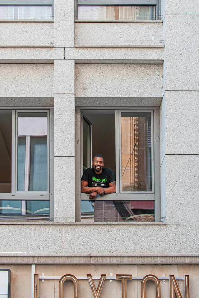 Ein junger Mann lehnt aus einem Fenster, darunter ein Leuchtschriftzug. Ein junger Mann lehnt aus einem Fenster, darunter ein Leuchtschriftzug.