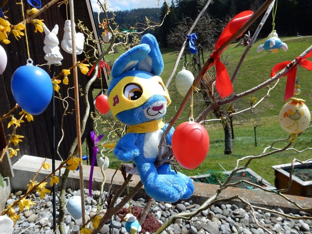 Plüschhase in Rennoutfit sitzt auf Osterbaum.