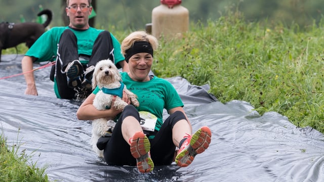 Eine Hundehalterin hält ihren kleinen Hund fest und rutscht auf einer Plastikplane den Hang herunter. Eine Hundehalterin hält ihren kleinen Hund fest und rutscht auf einer Plastikplane den Hang herunter.