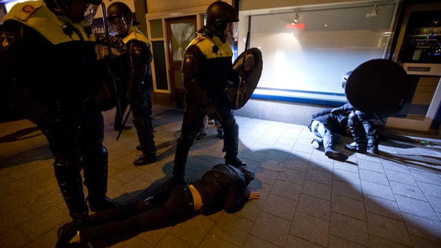 Polizisten stehen bei Personen, die auf dem Trottoir liegen. Polizisten stehen bei Personen, die auf dem Trottoir liegen.
