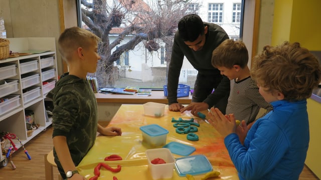 Drei Kinder und der Jugendliche an einem Tisch, auf dem die Kinder mit Knete Zahlen "schreiben". Drei Kinder und der Jugendliche an einem Tisch, auf dem die Kinder mit Knete Zahlen "schreiben".