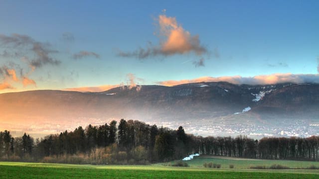 Rote Wolken bei Sonnenuntergang über einem Bergkamm, davor Wiese und Wald. Rote Wolken bei Sonnenuntergang über einem Bergkamm, davor Wiese und Wald.
