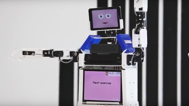 Ein Roboter hebt die Arme hoch. Eine Gruppe Rentner macht es ihm nach. Ein Roboter hebt die Arme hoch. Eine Gruppe Rentner macht es ihm nach.