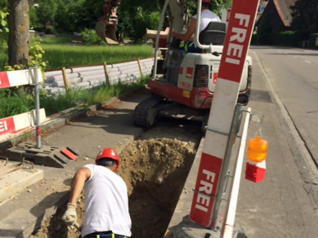 Ein Mann schaufelt, dahinter ein Bagger der eine Strasse aufreisst. Ein Mann schaufelt, dahinter ein Bagger der eine Strasse aufreisst.
