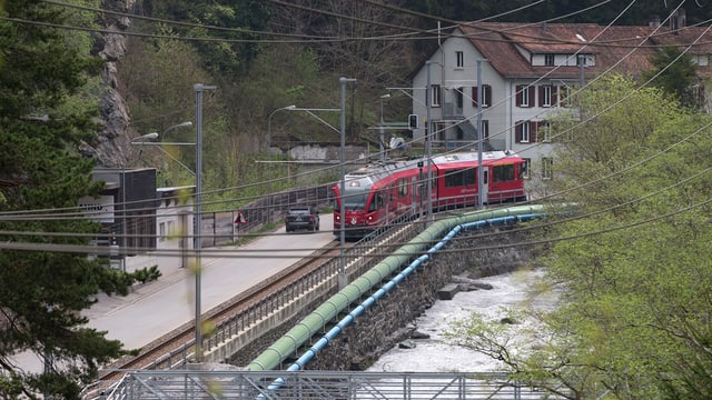 Ein Zug der RhB fährt neben der Strasse, die auf dem schmalen Talboden nach Meiersboden führt. Ein Zug der RhB fährt neben der Strasse, die auf dem schmalen Talboden nach Meiersboden führt.