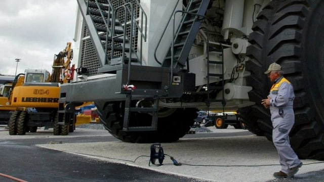 Liebherr-Mitarbeiter im grauen Overall vor schweren Maschinen der Marke Liebherr. Liebherr-Mitarbeiter im grauen Overall vor schweren Maschinen der Marke Liebherr.