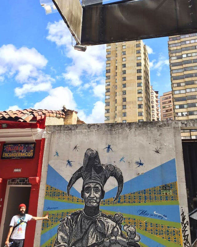 Ein Mann mit roter Mütze neben Graffiti, im Hintergrund Hochhäuser von Bogota. Ein Mann mit roter Mütze neben Graffiti, im Hintergrund Hochhäuser von Bogota.