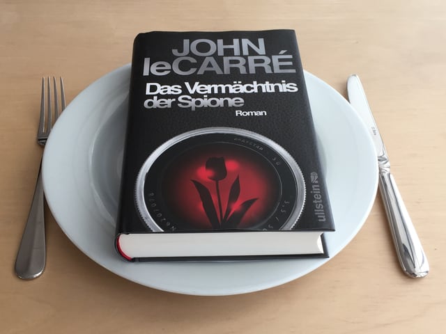 Der Roman «Das Vermächtnis der Spione» von John le Carré liegt auf einem weissen Teller. Messer und Gabel daneben. Der Roman «Das Vermächtnis der Spione» von John le Carré liegt auf einem weissen Teller. Messer und Gabel daneben.