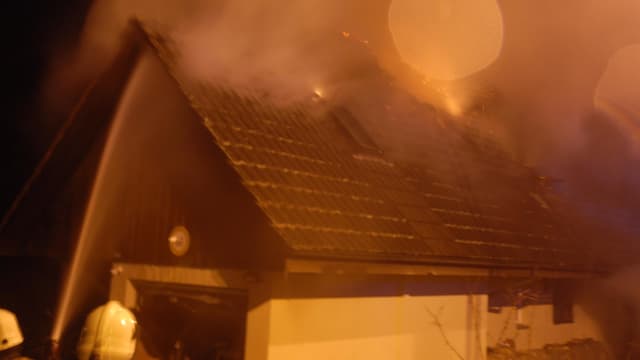 Feuerwehrmänner spritzen Wasser auf ein brennendes Hausdach. Feuerwehrmänner spritzen Wasser auf ein brennendes Hausdach.