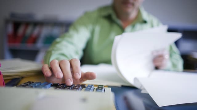 Ein Mann mit Papier an einem Rechner Ein Mann mit Papier an einem Rechner