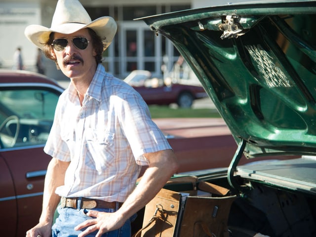 Ein Cowboy mit Hut lehnt ans Auto, der geöffnete Kofferraum hinter ihm. Ein Cowboy mit Hut lehnt ans Auto, der geöffnete Kofferraum hinter ihm.